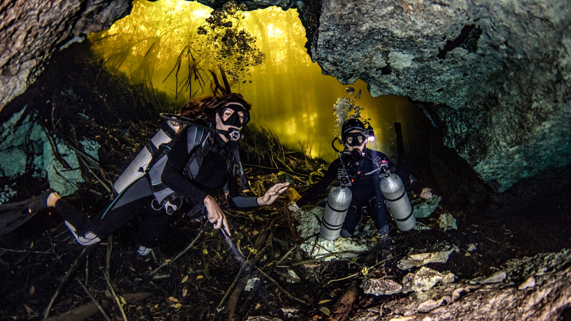 Two divers with lights communicating inside a cenote cave system